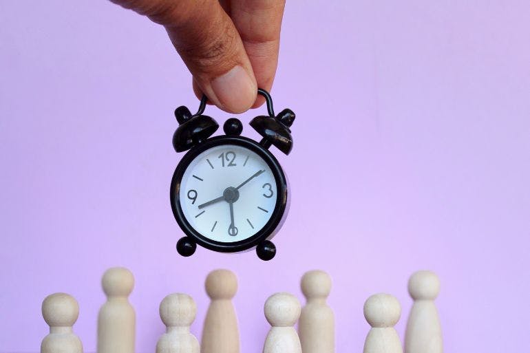 A clock held next to people figures symbolising employee clocking systems.