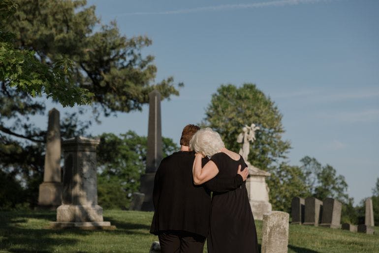 Two people embrace at a cemetery, comforting each other during a difficult time.