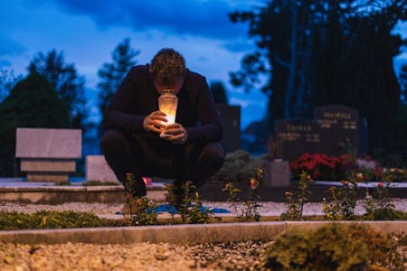 Bereavement Leave A man kneeling in front of a grave with a candle, symbolising grief and bereavement..