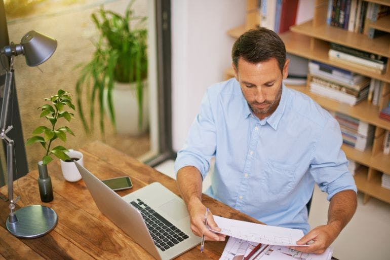 Man sitting at a desk with a laptop and papers, engaged in payroll record keeping.