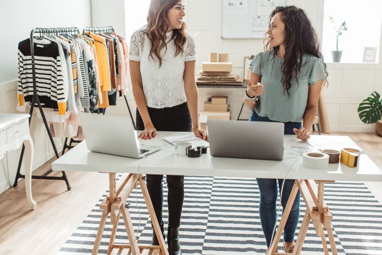 Two female business owners discussing over a desk if they need a payroll solution.