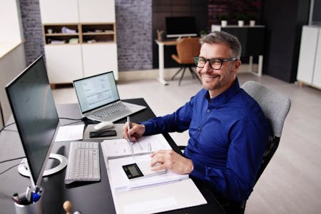 payroll accounting Man in a blue shirt sitting at his desk with a laptop, working on payroll accounting.