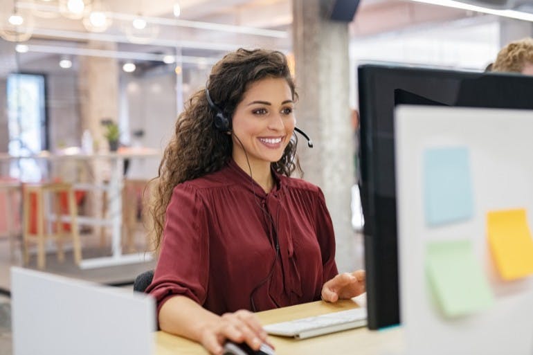 Female outsourced payroll services employee helping client on the phone wearing headset.