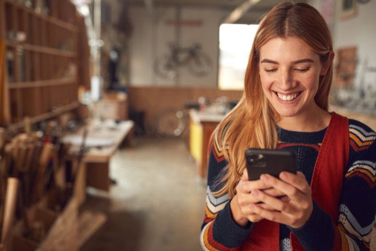 Female owner of a bicycle repair shop using an HR app on phone in her shop.