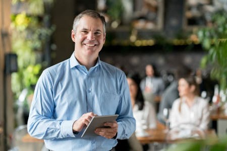 HR app Male business owner using an HR app on a tablet in a resturant