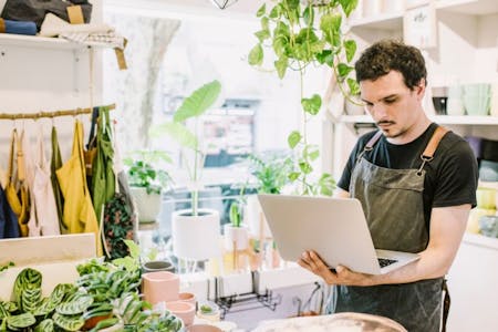 SaaS HRIS Business owner using an HRIS system on his laptop in plant shop.