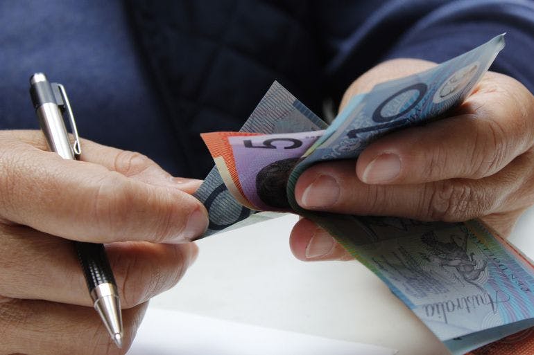 Male business owner holding a pen and Australian dollars, cashing out annual leave.