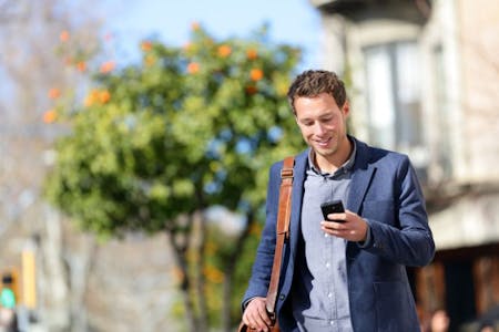 HR apps Male employer in a suit walking down the street using an HR app on his phone.