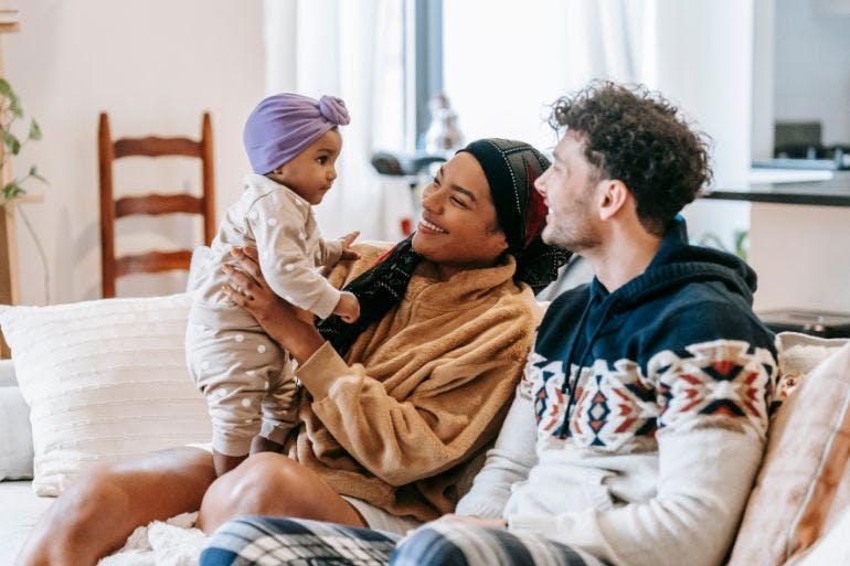 A couple and their baby on couch on shared parental leave