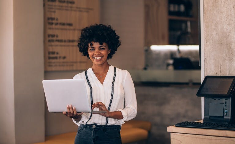 Female restaurant owner smiling holding a laptop, happy using payroll software.