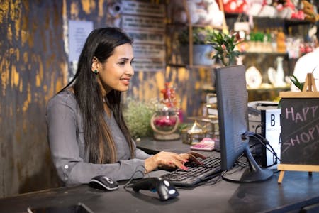 Is a payroll accountant needed for small businesses Female small business owner using payroll software on a computer in her store.