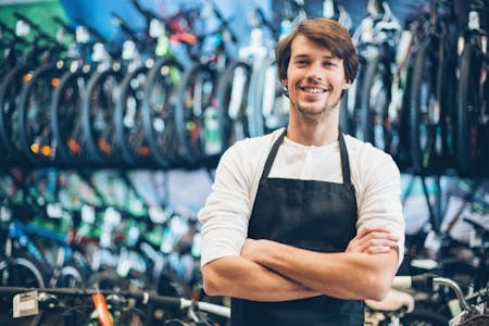 Is a payroll accountant needed for small businesses Male business owner of a bicycle shop standing with his arms crossed smiling.
