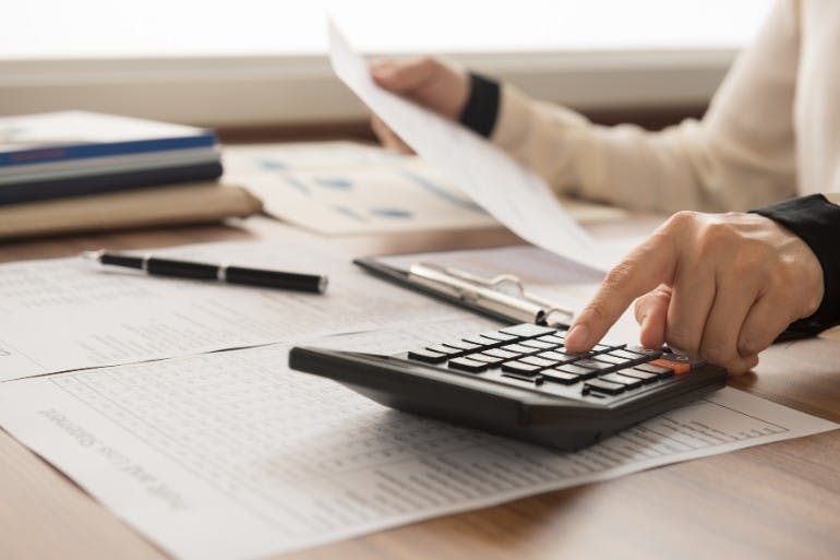 Woman using calculator to determine finances, factoring in payroll deductions.