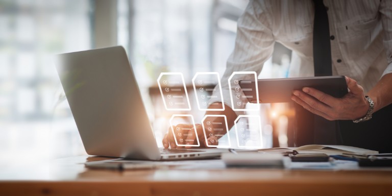 man efficiently manages documents using a laptop and tablet on a desk, showcasing modern technology in action.