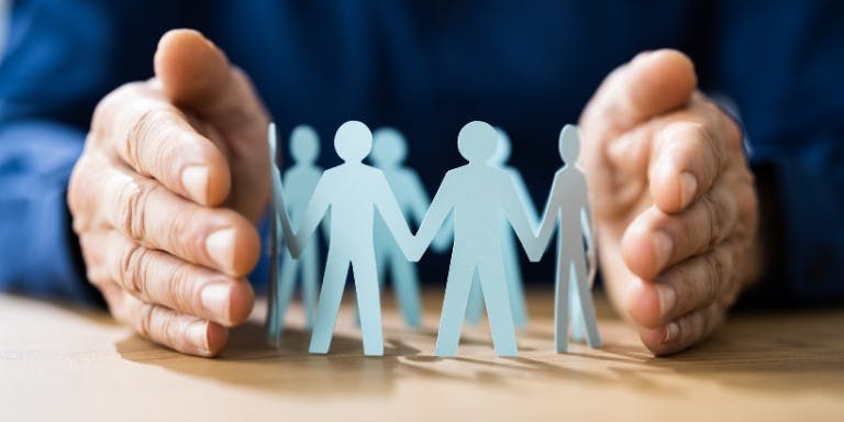 Keeping staff safe Hand around paper figures symbolising protecting staff