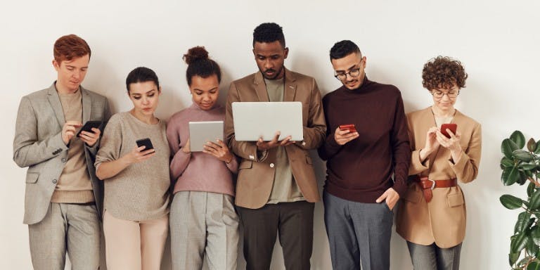 Difference between HRIS and HRMS team of professionals stands against a white wall, each using their laptops, symbolising modern collaboration with HRIS and HRMS
