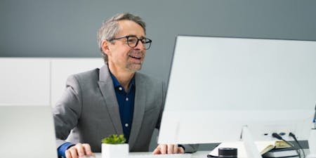 man with glasses smiles at a computer screen, showcasing the user-friendly interface of a document management system.