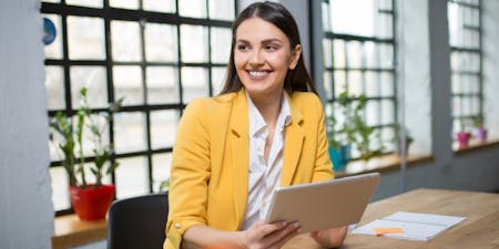 woman in a yellow jacket sits at a table, using a tablet to manage documents efficiently.