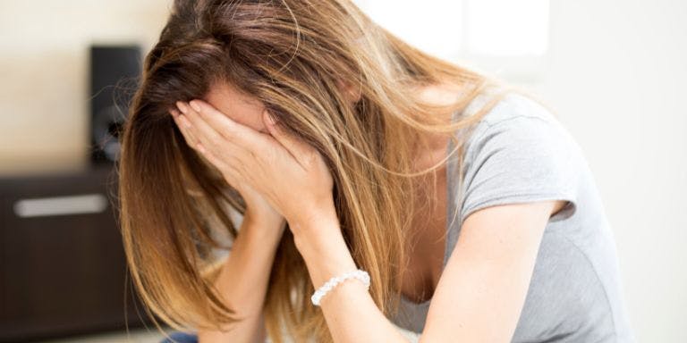 woman sits on the floor, hands on her face, reflecting the message of compassion during Don't Be a Bully Month.
