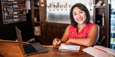 Paying wages Female business owner of a bar smiling using payroll software to mange wages