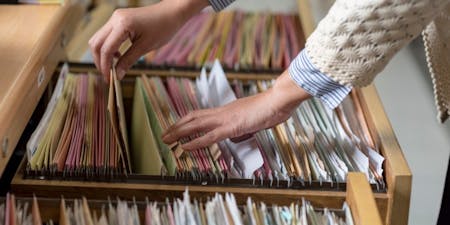 Types of HR documents An individual extracting HR documents from a drawer, highlighting the management of essential human resources paperwork.