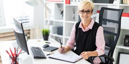Employee documentation Woman in glasses is seated at a desk, working on her computer with employee documentation nearby.