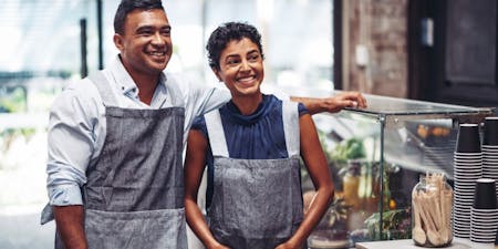 Pay and benefits in Australia Male and female employee smiling as they get fair pay and employee benefits in a cafe.
