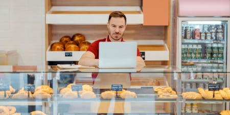 HR data analytics Male business owner analyzes HR data on laptop in his bakery.