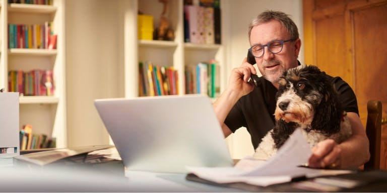 Man with glasses working on laptop, accompanied by his dog, representing the idea of flexible working arrangements.