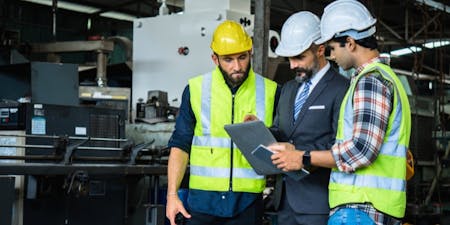 Health and Safety at Work Act Three men wearing hard hats in front of a factory, highlighting the importance of safety regulations under the Health and Safety at Work Act