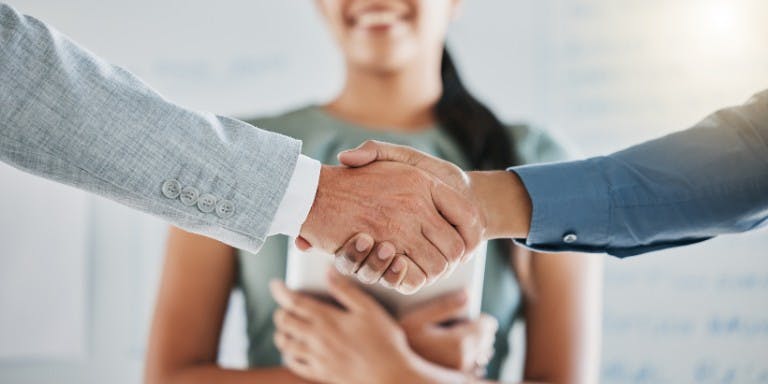 Two business individuals shaking hands in an office setting, representing the completion of onboarding documents and partnership.