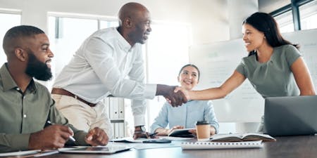 Business professionals shaking hands during a meeting, symbolizing agreement and collaboration on onboarding documents.