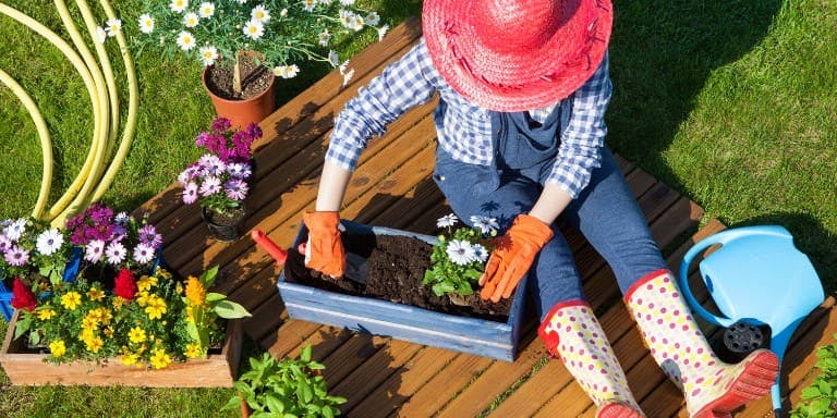 A woman sits in a serene garden, surrounded by greenery, holding gardening tools, symbolyising garden leave from work.