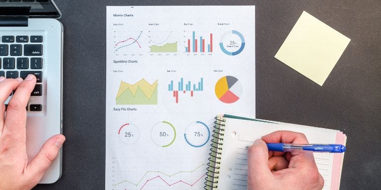 Person with a laptop and paper graph with statistical analysis and a notepad and pen