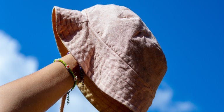 A hand holding out a bucket hat in front of a blue sky