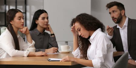 Types of discrimination Woman with her head in her hands at a table, illustrating the emotional strain caused by discrimination in the workplace.