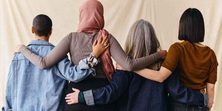 Four women stand together, arms linked, embodying support and resilience in addressing workplace discrimination issues.