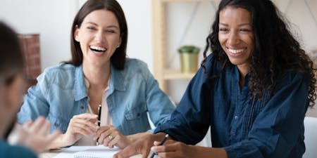 employee engagement Two women laughing at a meeting, showing high employee engagement.