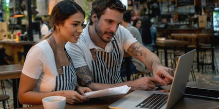 Staff scheduling Business owners review staff schedule on a laptop while seated at in their restaurant.