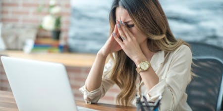 Workplace direct discrimination Woman with her head in her hands at her desk, illustrating the emotional toll of workplace discrimination.