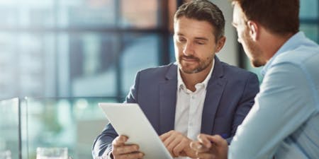 Two professionals in business attire engage in a discussion about employee discipline at a table with a tablet