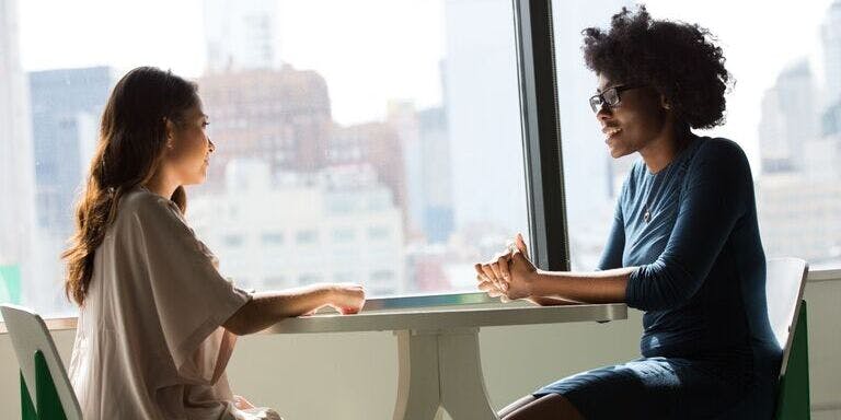 Disciplinary at work Two women seated at a table, conversing about disciplinary issues in a professional setting.