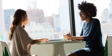 Disciplinary at work Two women seated at a table, conversing about disciplinary issues in a professional setting.