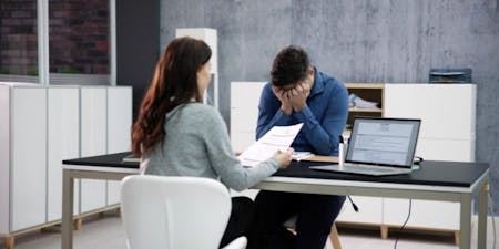 Disciplinary at work Man and woman sit at a desk, reviewing papers during a workplace disciplinary meeting.