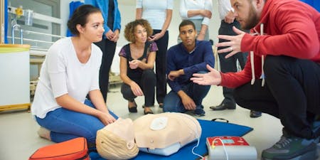 First aid at work Team of employees collaborates around a mannequin, practicing first aid techniques in a work environment.