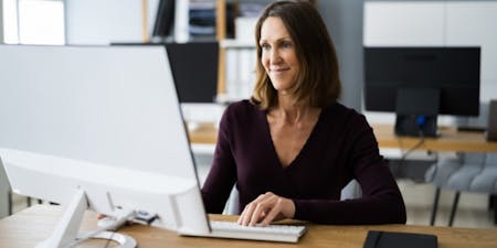 Payrolling benefits in kind Woman in an office at a desk using a computer to payroll tax benefits.