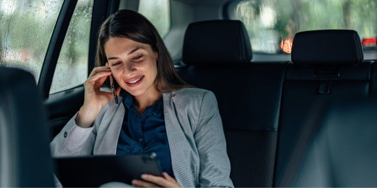Business women in a company car, on the phone using a tablet,