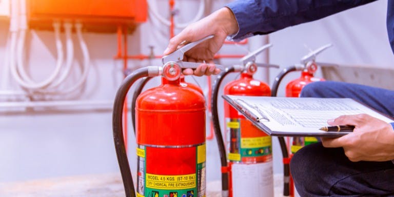 Man reviews fire extinguishers with a clipboard in hand, focusing on ensuring fire safety standards at work.