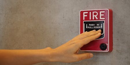 Fire safety at work Person pressing a fire alarm button on a wall, highlighting workplace fire safety measures and emergency preparedness.