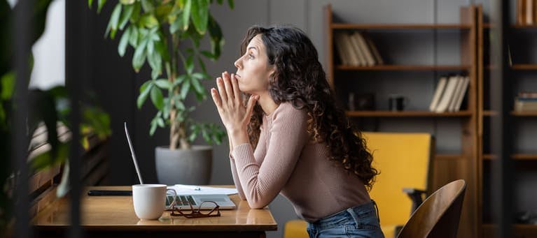 A woman looking stressed at her desk with a laptop in front of her